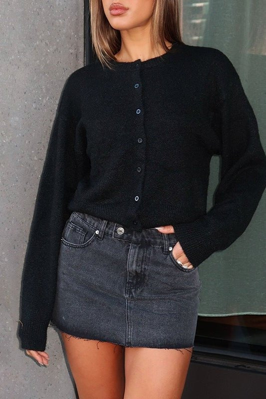 Schwarze kurze Strickjacke zugeknöpft, zu einem Jeans-Minirock getragen