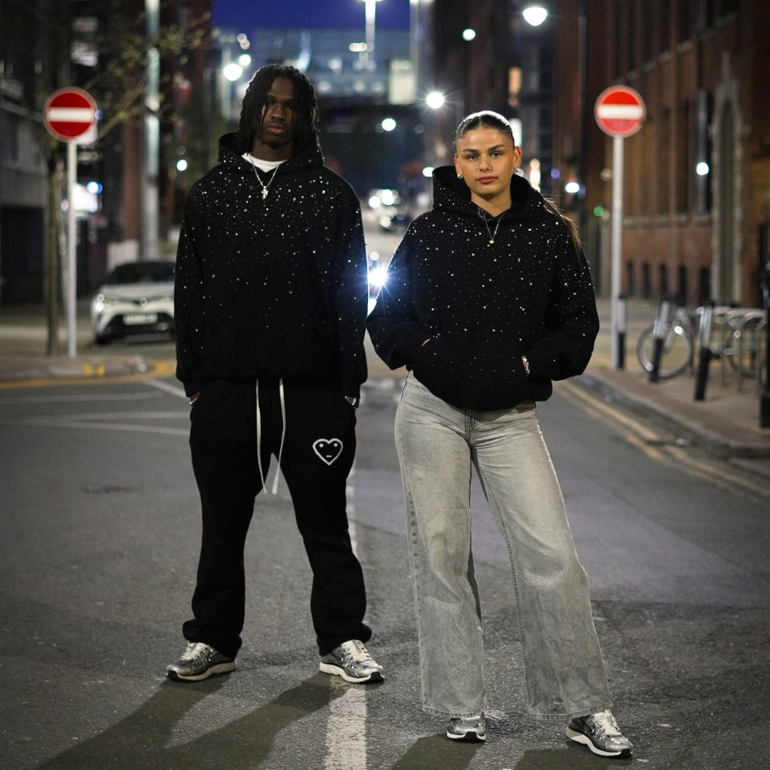 Schwarzer Oversize-Hoodie mit Strass, getragen von einem Mann und einer Frau nachts in der Stadt