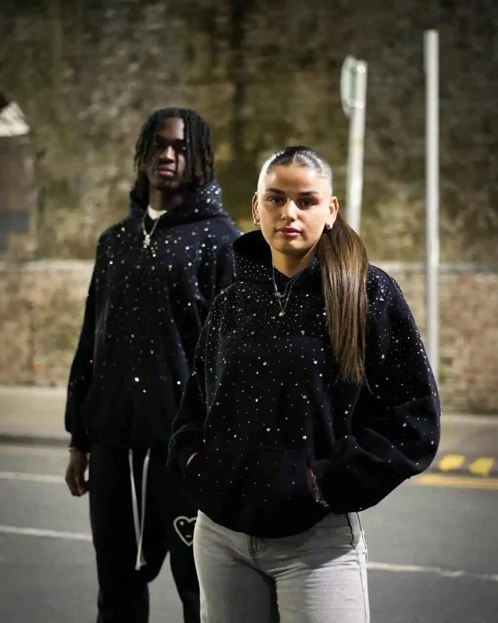 Ein Mann und eine Frau im schwarzen Oversize-Hoodie mit Strasssteinen
