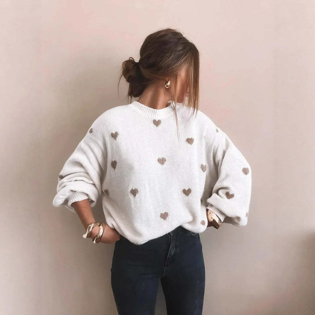Weißer Oversize-Pullover mit eingestrickten beigefarbenen Herzen, zu dunkler Jeans getragen