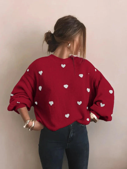Roter Oversize-Herzpullover zu dunkler Jeans, Hände in die Hüften gestemmt