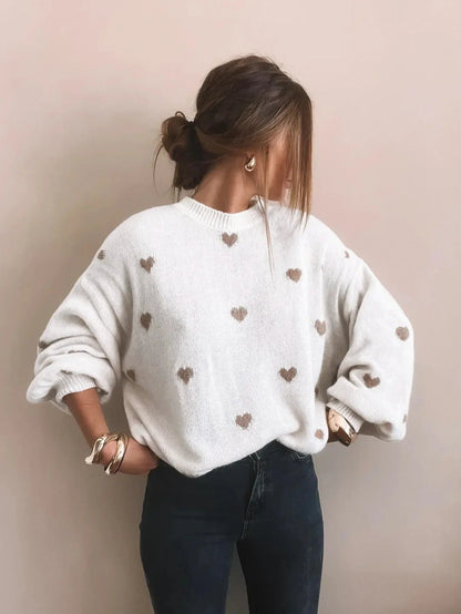 Weißer Oversize-Herzpullover mit beigefarbenen Herzen, Hände in die Hüften gestemmt