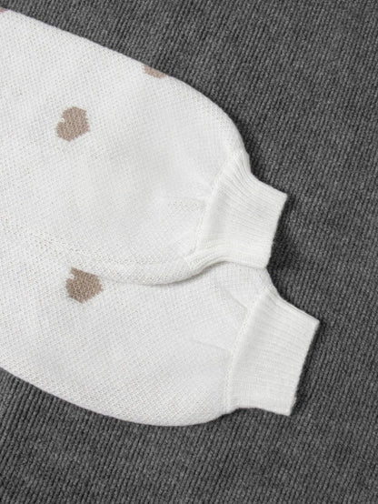 Nahaufnahme der Rippbündchen an den Ärmeln des weißen Herzpullovers