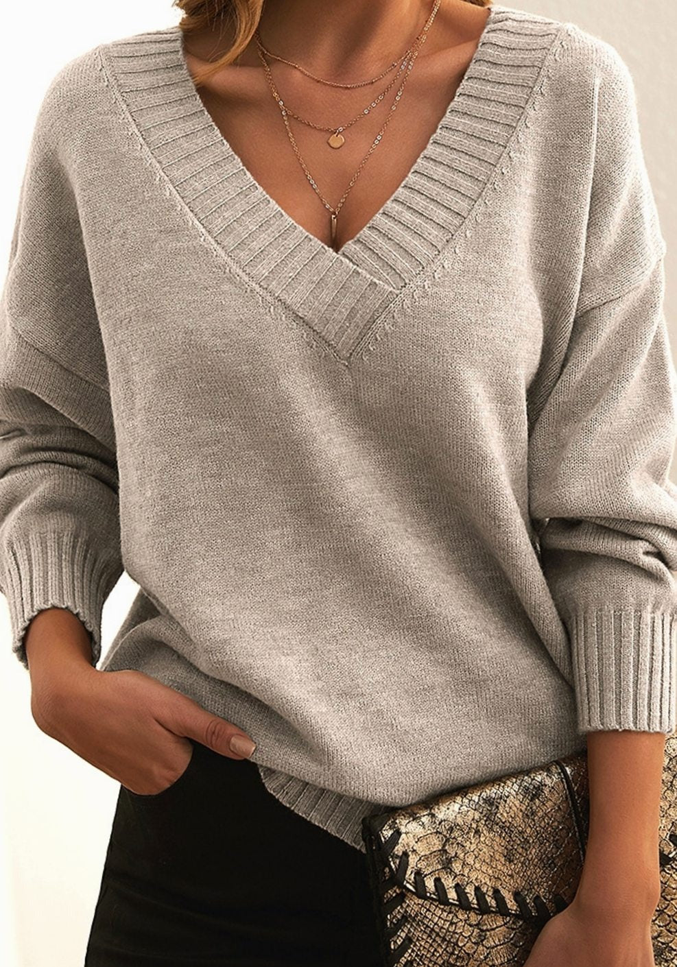 Beigefarbener Pullover mit V-Ausschnitt zu schwarzer Hose und Clutch mit Schlangenmuster